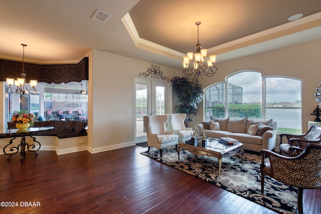 living room featuring a tray ceiling, dark wood-type flooring, a healthy amount of sunlight, and a notable chandelier