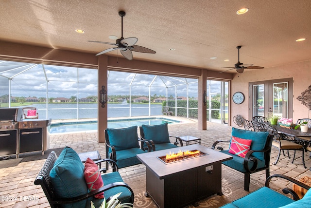 view of patio featuring glass enclosure, ceiling fan, and an outdoor living space with a fire pit