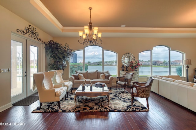 living room with a water view, dark hardwood / wood-style floors, a tray ceiling, and an inviting chandelier