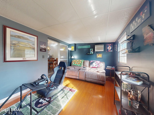 living area featuring a wall mounted AC, a drop ceiling, wood finished floors, and a wall mounted air conditioner