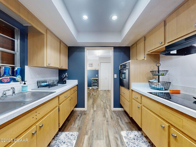 kitchen with light wood finished floors, light countertops, wall oven, a sink, and black electric cooktop