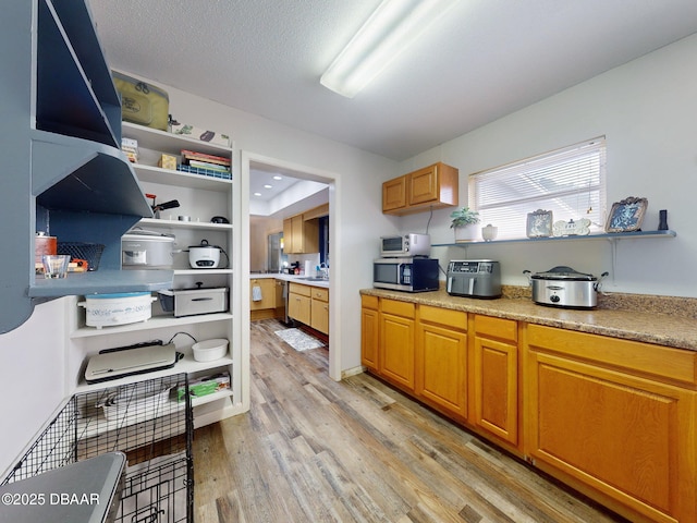 kitchen with stainless steel microwave, brown cabinets, light countertops, a textured ceiling, and light wood-style floors