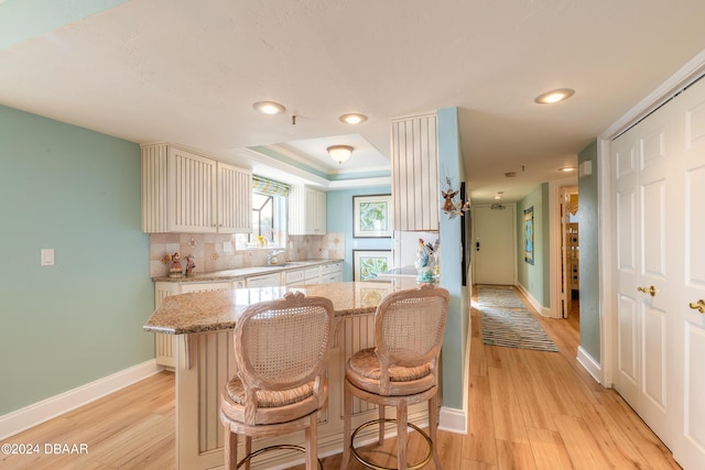 kitchen with sink, light stone counters, backsplash, light hardwood / wood-style floors, and a breakfast bar