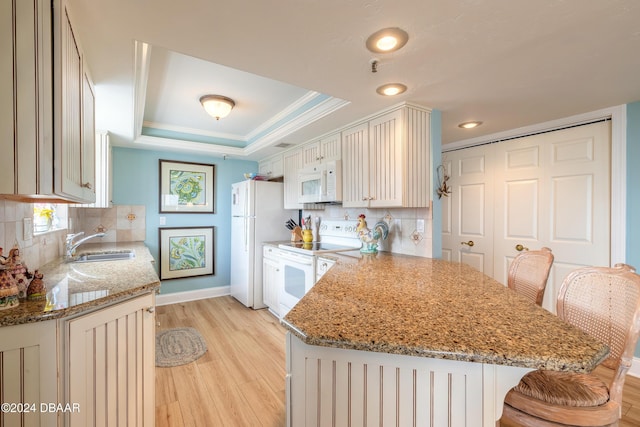 kitchen with light wood-type flooring, white appliances, a tray ceiling, sink, and stone countertops