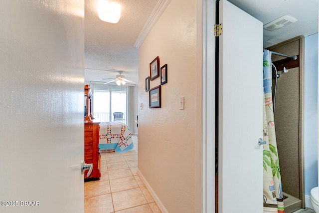 hall featuring crown molding, light tile patterned floors, visible vents, a textured ceiling, and baseboards