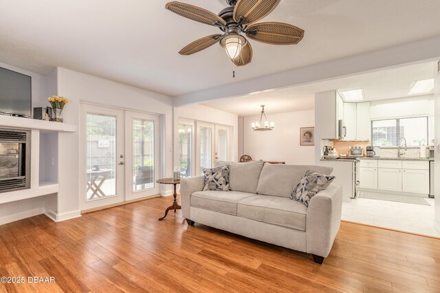 living room featuring light wood finished floors, a chandelier, french doors, and a ceiling fan