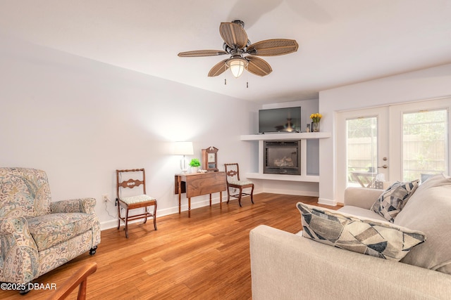 living room featuring light wood-style floors, a ceiling fan, baseboards, french doors, and a glass covered fireplace