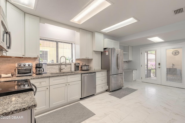 kitchen with stainless steel appliances, a sink, light marble finish flooring, backsplash, and white cabinets