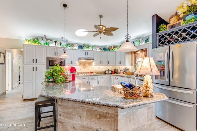 kitchen featuring a kitchen bar, stainless steel appliances, light hardwood / wood-style floors, white cabinets, and pendant lighting