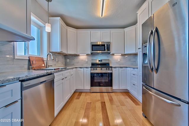 kitchen featuring stainless steel appliances, a sink, white cabinetry, light wood-style floors, and decorative backsplash