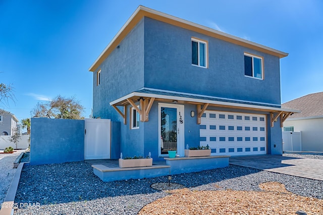 view of front of house featuring an attached garage, a gate, decorative driveway, and stucco siding