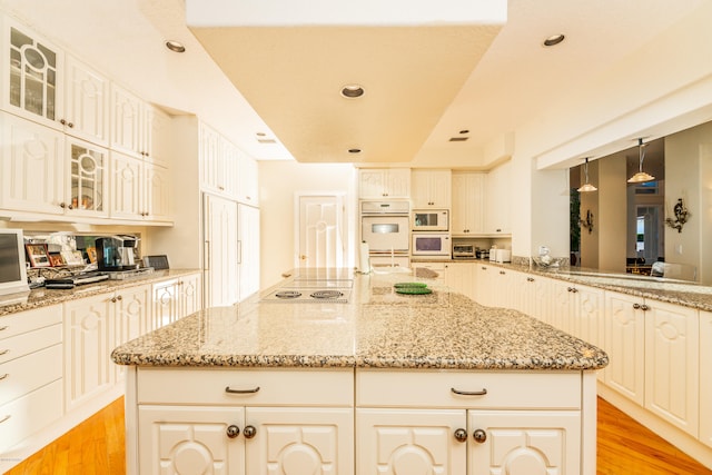 kitchen with light stone counters, decorative light fixtures, white appliances, light hardwood / wood-style flooring, and a center island