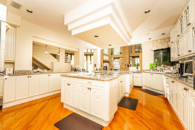 kitchen featuring white cabinets, sink, a kitchen island with sink, and light hardwood / wood-style flooring