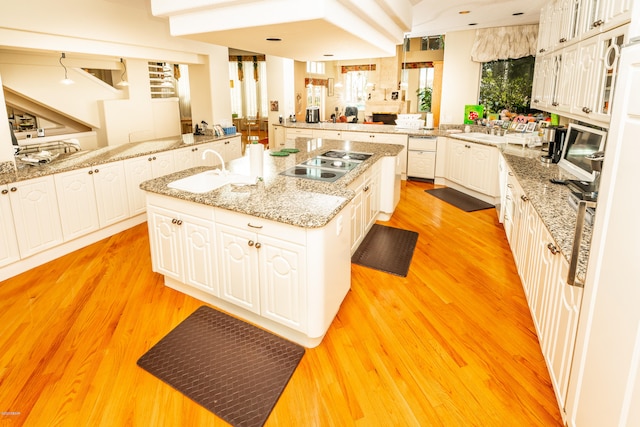 kitchen with white cabinetry, light wood-type flooring, black electric stovetop, and an island with sink