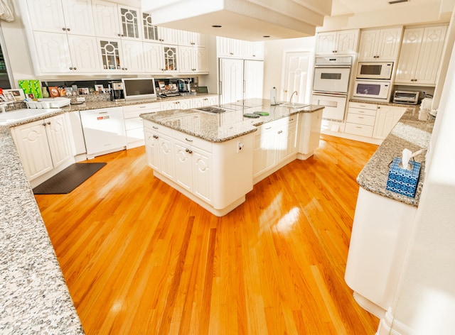 kitchen with white appliances, light stone counters, light hardwood / wood-style floors, and white cabinets