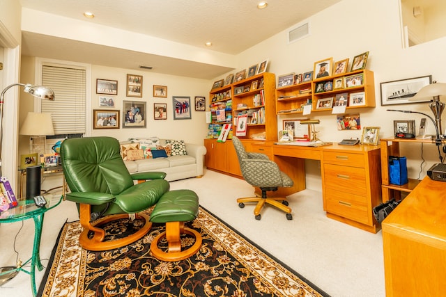 carpeted office with a textured ceiling and built in desk