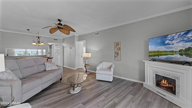 living room with a premium fireplace, hardwood / wood-style flooring, ornamental molding, and ceiling fan with notable chandelier