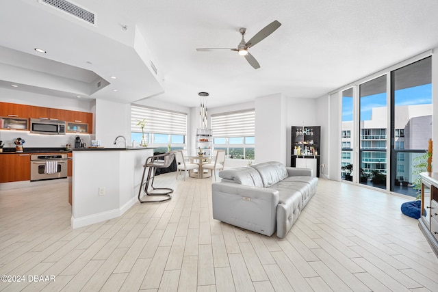 living room with light wood-type flooring, sink, and ceiling fan with notable chandelier