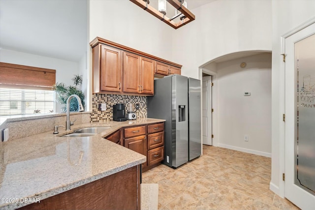 kitchen featuring sink, stainless steel fridge, light stone countertops, decorative backsplash, and a high ceiling