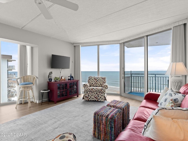 living area with wood finished floors, a textured ceiling, healthy amount of natural light, a ceiling fan, and a wall of windows