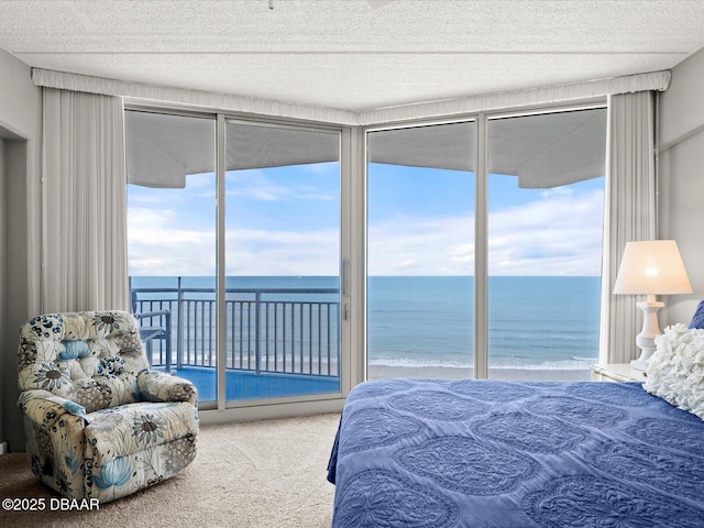 bedroom with access to outside, view of water and beach, carpet flooring, floor to ceiling windows, and a textured ceiling