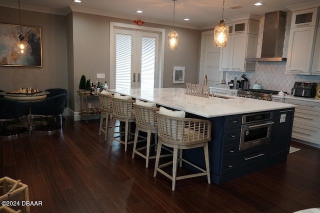 kitchen with wall chimney exhaust hood, stainless steel appliances, dark hardwood / wood-style flooring, pendant lighting, and white cabinets