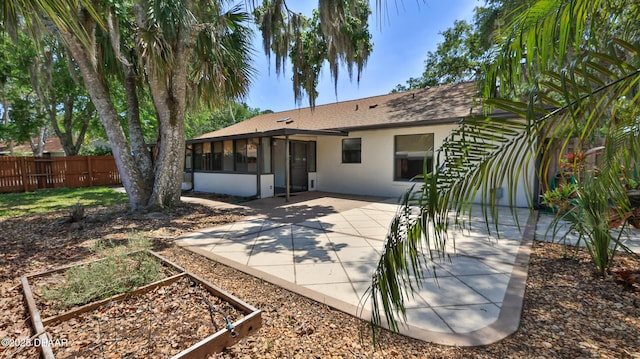 rear view of property with stucco siding, a garden, fence, a patio, and a sunroom