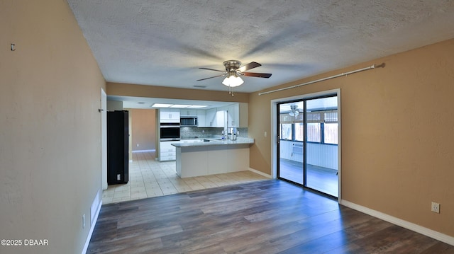kitchen with wood finished floors, appliances with stainless steel finishes, backsplash, a ceiling fan, and a textured ceiling