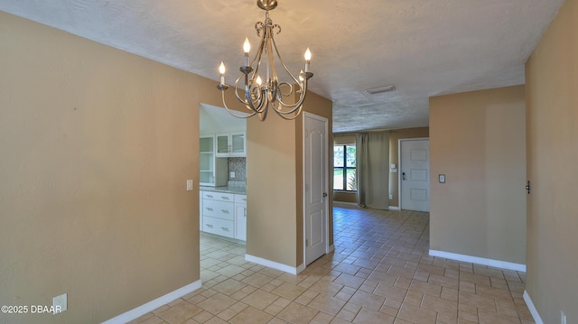 empty room featuring a textured ceiling, visible vents, a chandelier, and baseboards