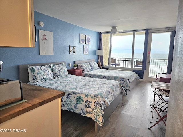 bedroom featuring access to exterior, ceiling fan, a water view, and wood-type flooring