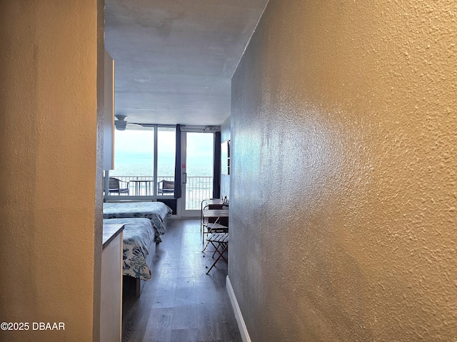 corridor with a water view, floor to ceiling windows, and dark wood-type flooring