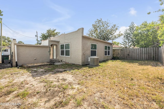 back of property with a fenced backyard, stucco siding, central AC unit, entry steps, and a yard