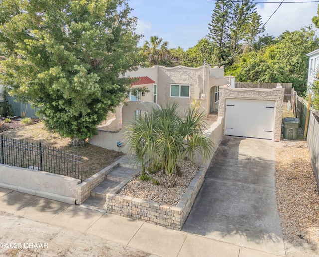 view of front facade featuring an attached garage, a fenced front yard, stucco siding, and driveway