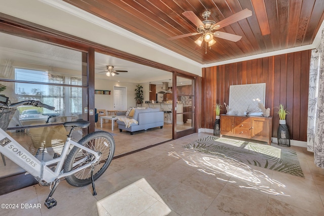 living room featuring ornamental molding, wooden ceiling, wood walls, and baseboards