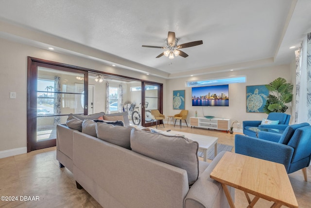 living room featuring ceiling fan, a textured ceiling, a raised ceiling, and baseboards