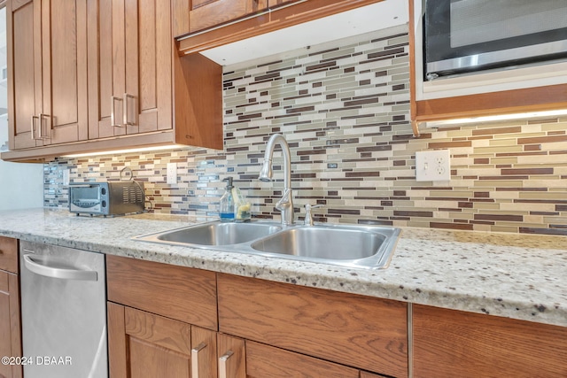 kitchen featuring appliances with stainless steel finishes, brown cabinetry, a sink, and tasteful backsplash