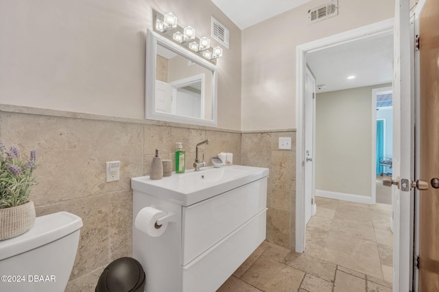 half bath with toilet, visible vents, tile walls, and vanity