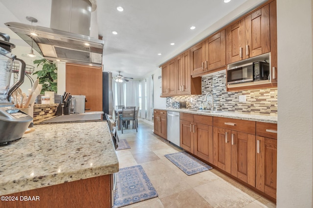 kitchen with light stone counters, appliances with stainless steel finishes, a ceiling fan, a sink, and island range hood