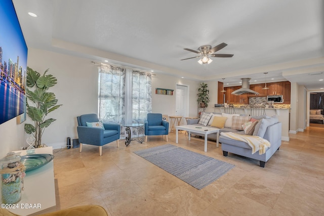 living area featuring a tray ceiling, recessed lighting, a ceiling fan, and baseboards