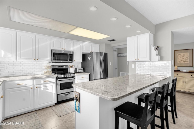 kitchen featuring white cabinets, a kitchen breakfast bar, stainless steel appliances, and light stone counters