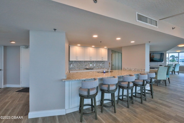 kitchen with hardwood / wood-style flooring, decorative backsplash, light stone countertops, white cabinets, and a breakfast bar