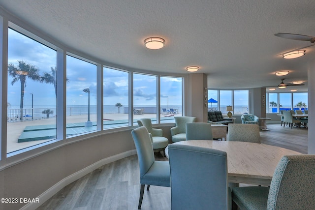 dining space with a textured ceiling, ceiling fan, a water view, and hardwood / wood-style floors