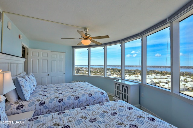 bedroom with a textured ceiling, a closet, a water view, and ceiling fan