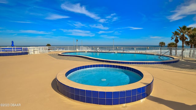 view of swimming pool with a patio area, a water view, and a hot tub