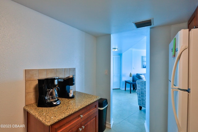 kitchen with light tile patterned floors, white refrigerator, and light stone counters