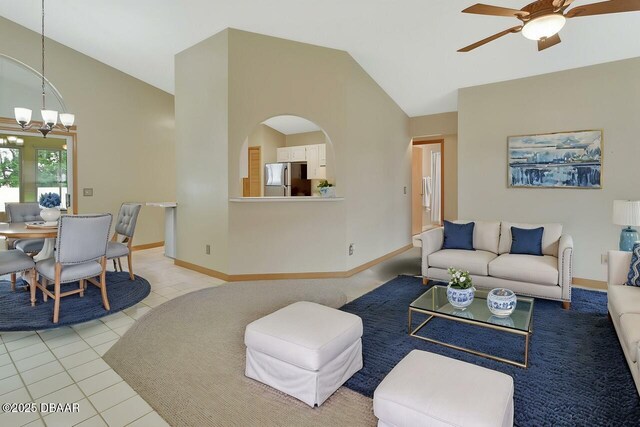 living room with lofted ceiling, light tile patterned floors, arched walkways, baseboards, and ceiling fan with notable chandelier