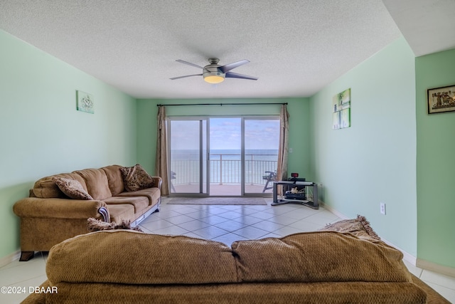 living room featuring ceiling fan, light tile patterned floors, a water view, and a textured ceiling