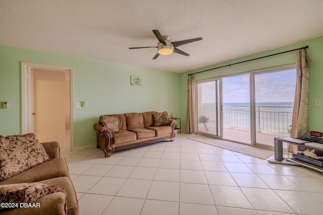 tiled living room featuring ceiling fan, a water view, and a textured ceiling