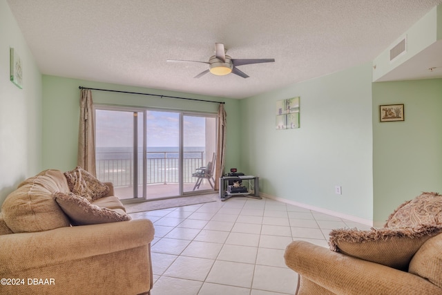 living room featuring a water view, ceiling fan, light tile patterned floors, and a textured ceiling