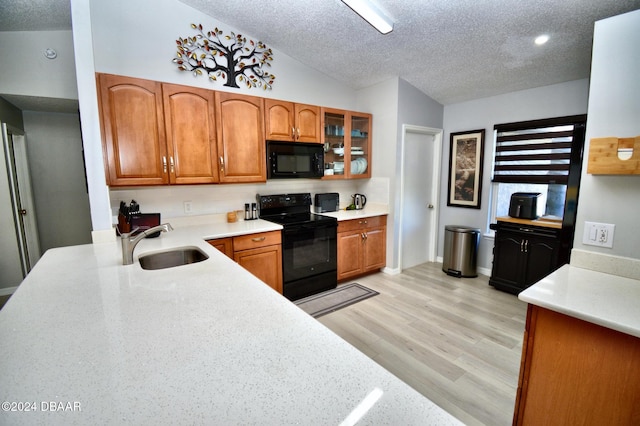 kitchen with vaulted ceiling, sink, black appliances, a textured ceiling, and light hardwood / wood-style flooring